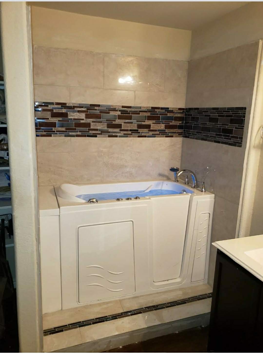 Finished walk-in therapeutic tub with travertine tile surround and glass mosaic accent band
