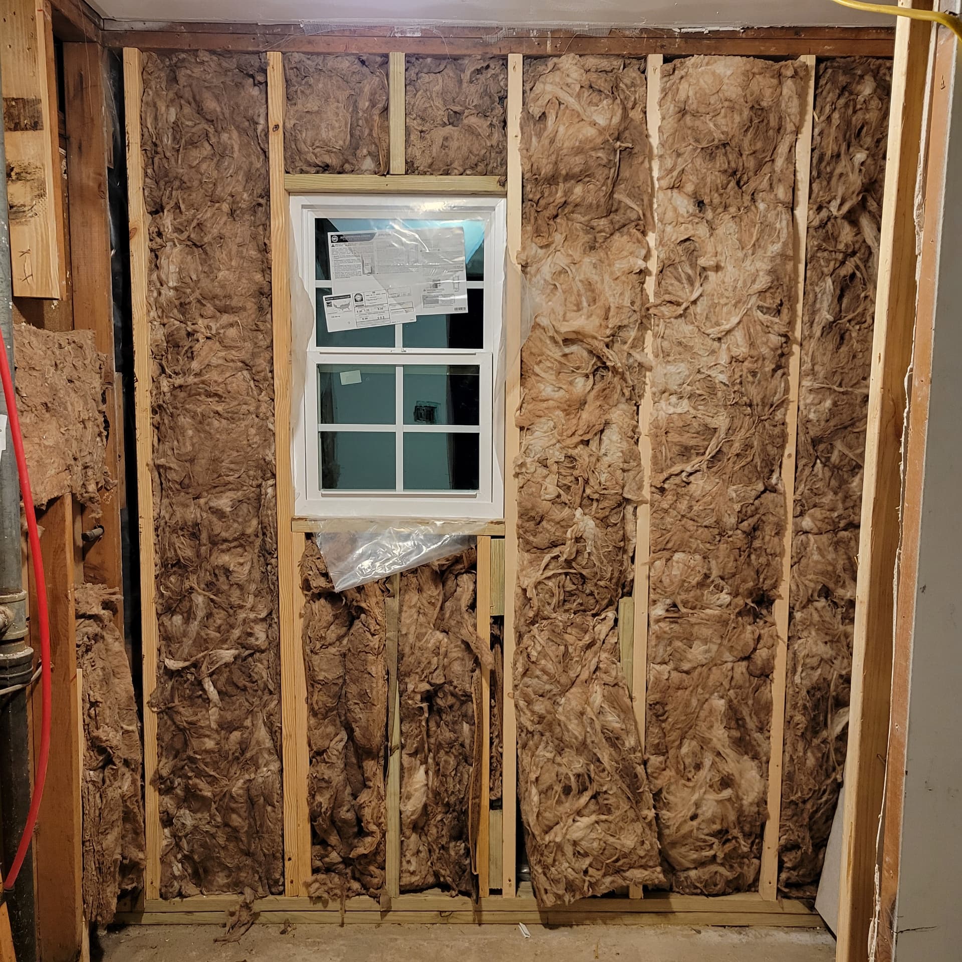 Wall framing opened up with fiberglass insulation and a newly installed four-pane window during remodel