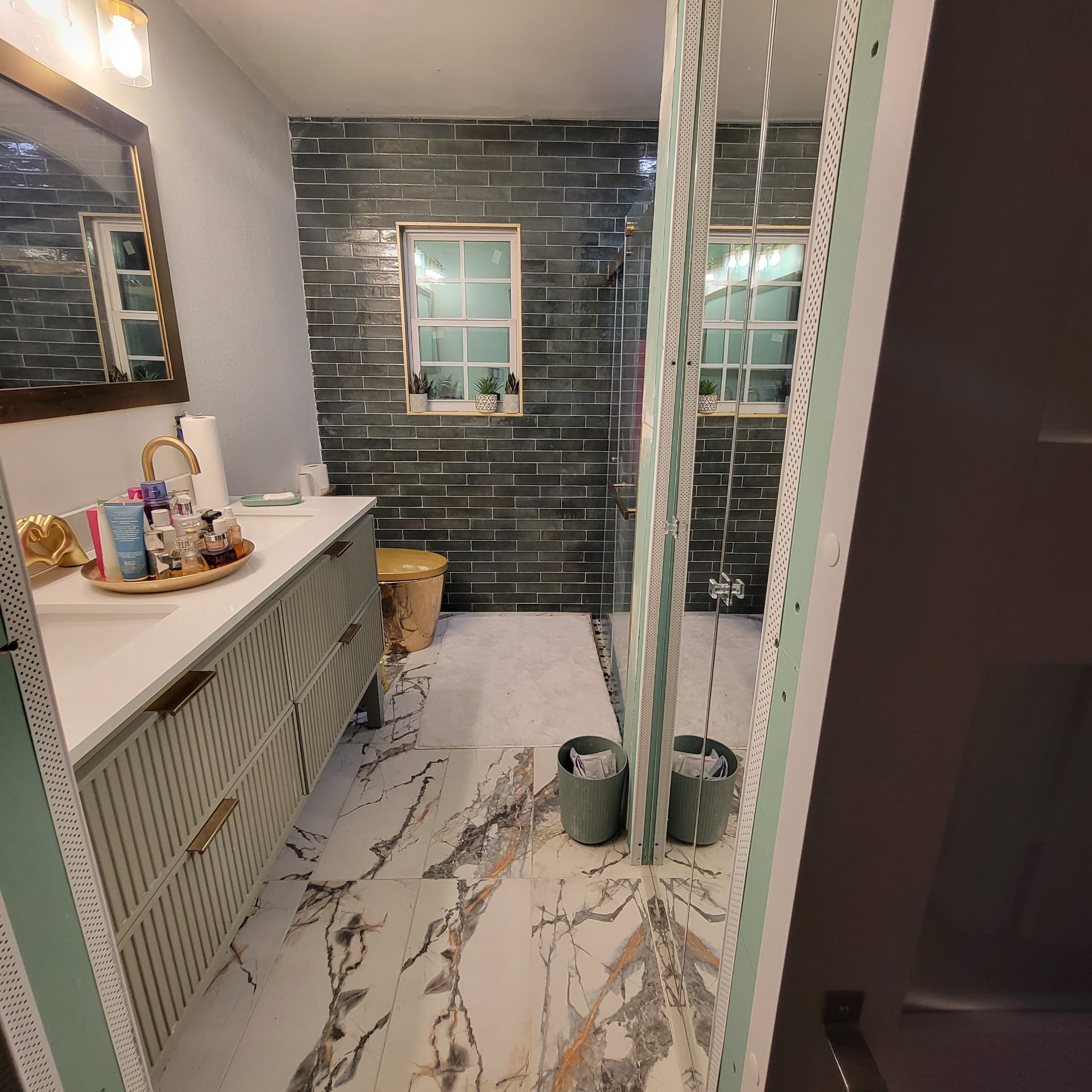Finished bathroom with sage green slatted vanity, gold faucet and a matching gold toilet over white marble-look floor tile