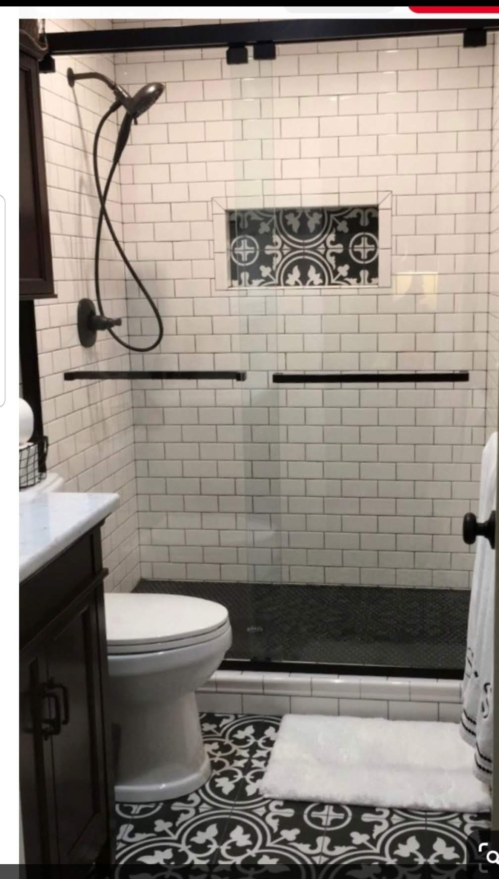 Walk-in shower with white subway tile, black hardware, decorative mosaic niche and patterned floor tile