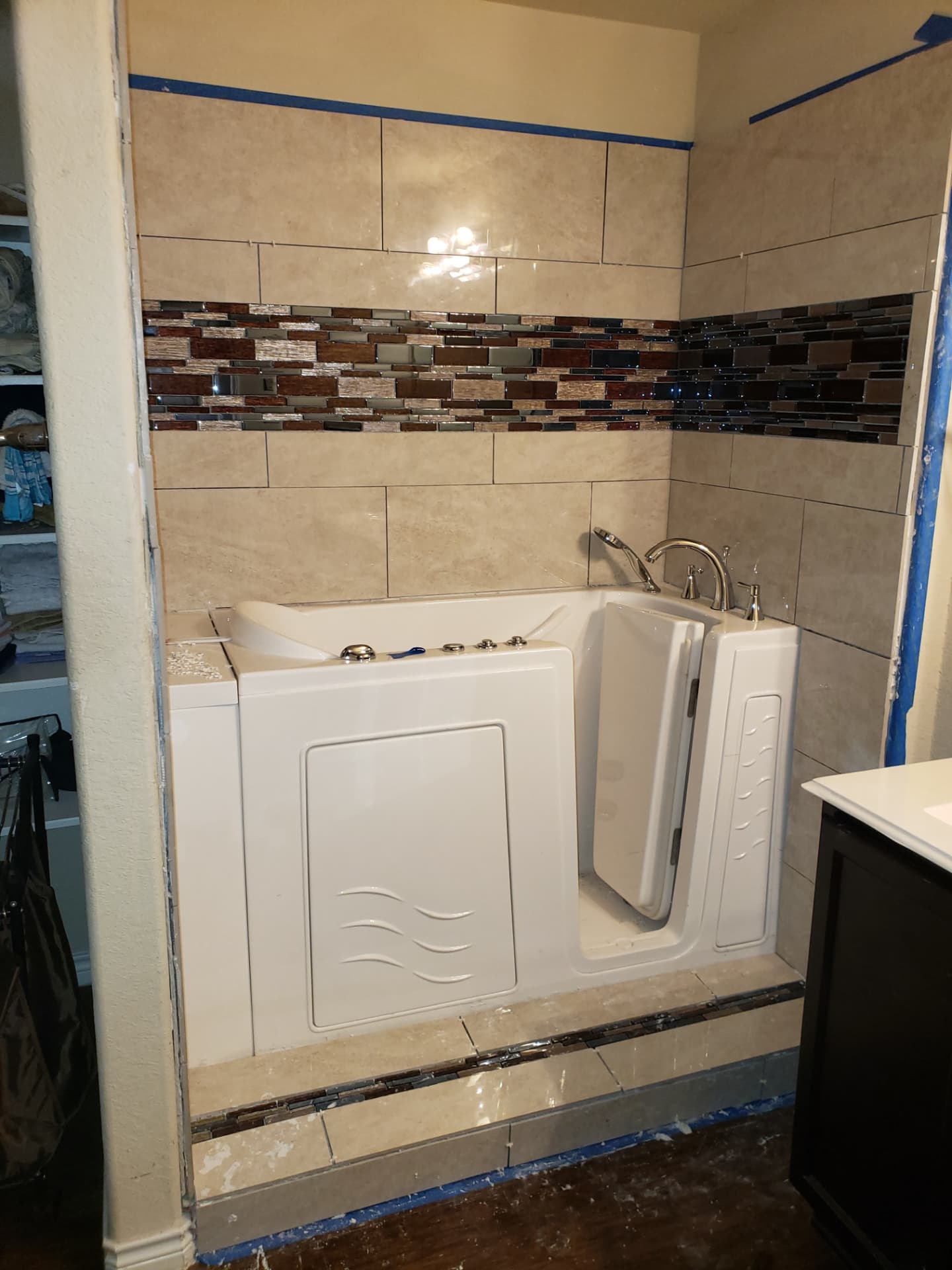 Walk-in tub surround mid-installation with fresh tile and blue painter's tape