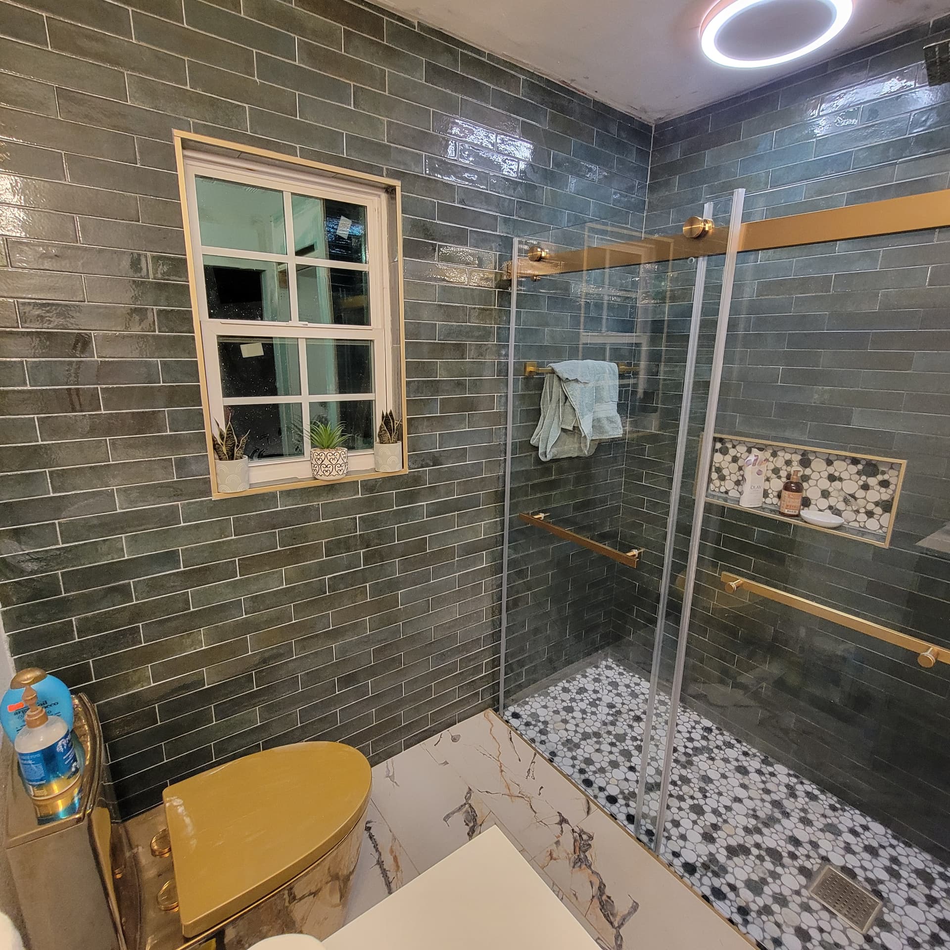 Finished bathroom with dark green glossy subway tile walk-in shower, gold hardware, penny-tile shower floor and marble-look floor tile