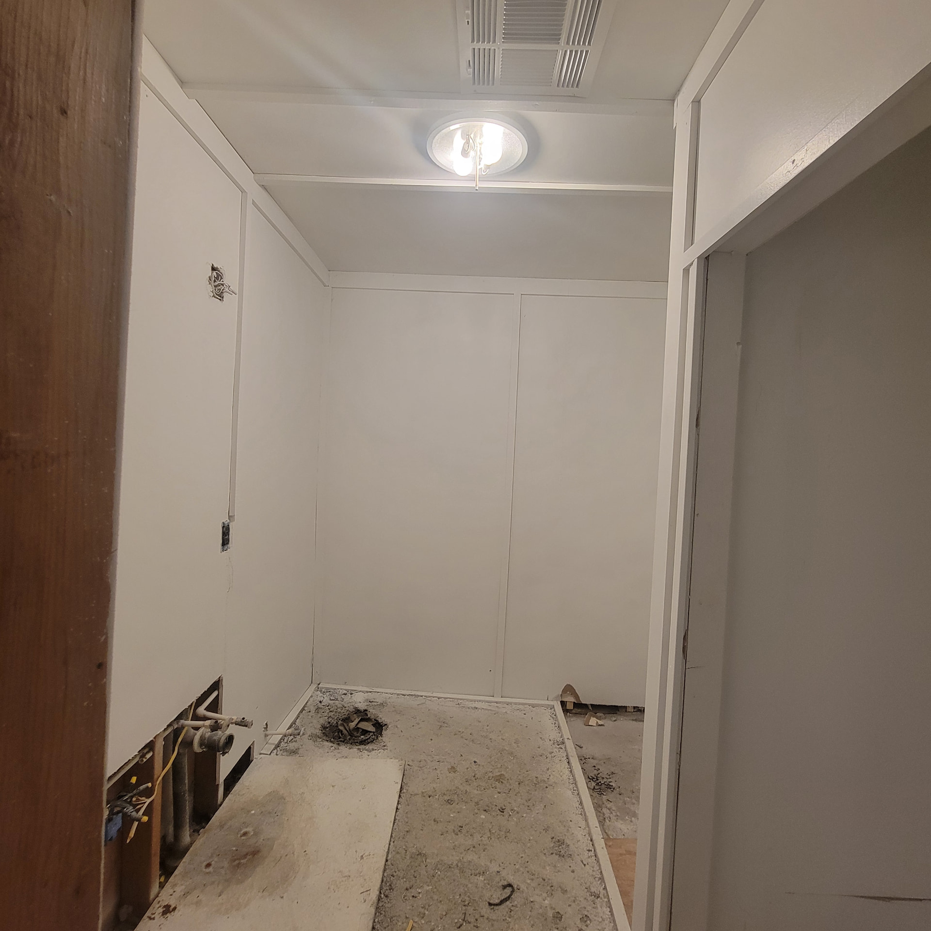 Bathroom demolition stage with bare concrete subfloor, exposed drain and plumbing rough-ins for a vanity